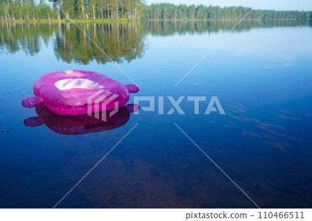 A pink children's swimming circle on the water of a calm lake. A pink children's swimming circle on the water of a calm lake. 110466511