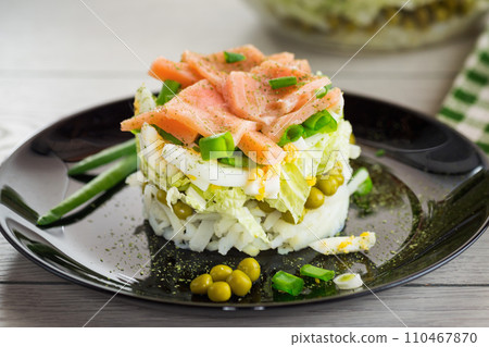 Layered salad of cabbage and other vegetables with pieces of red fish in a plate. Layered salad of cabbage and other vegetables with pieces of red fish in a plate. 110467870