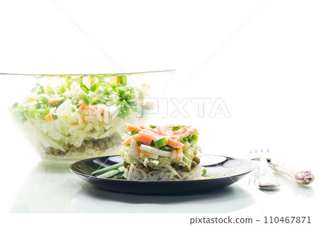 Layered salad of cabbage and other vegetables with pieces of red fish in a plate. 110467871