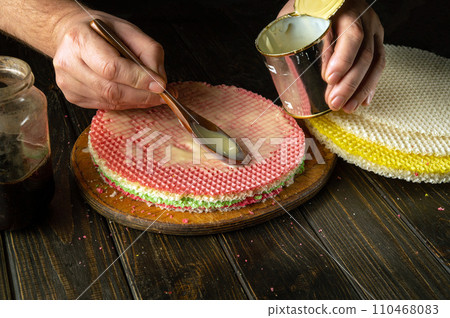The cook is preparing a delicious waffle cake with jam and condensed milk for a festive dinner. Vintage spoon in chef hand 110468083