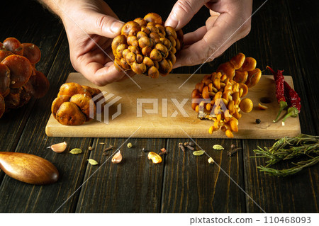 Chef preparing fresh velvet shank mushrooms on the kitchen table with aromatic spices and rosemary. Sorting wild enoki mushrooms by the hands of a cook 110468093