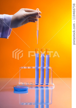 Professional scientist is dripping some liquid from a pipette to few test tubes displayed on a rack. A petri dish with blue chemical featured. Testing modern technological tools 110468738