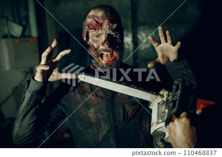 Walking zombie dead man and chainsaw attack on horror halloween party. 110468837