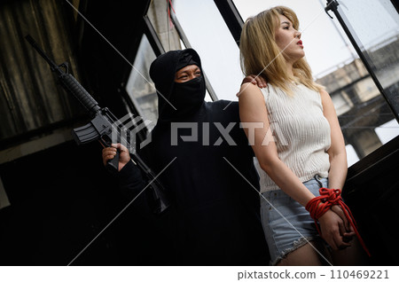 Kidnapper with gun and women hostages standing looking out of window 110469221