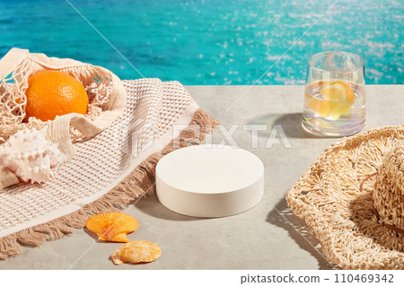 White podium in round shaped arranged with a hat, a cup of water and a mesh bag containing an orange. Minimal podium display for cosmetic product presentation White podium in round shaped arranged with a hat, a cup of water and a mesh bag containing an orange. Minimal podium display for cosmetic product presentation 110469342