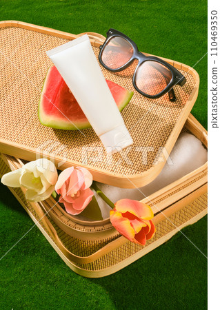 Picnic basket containing folded towel and some tulip flowers inside. A sunglasses, a slice of watermelon and unbranded tube displayed. The concept of summer vacation, skin and face care 110469350