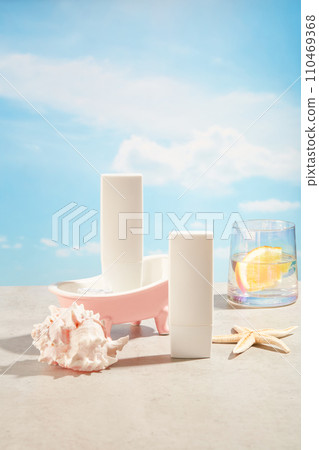 Two blank label bottles in white color decorated with starfish, conch shell and a cup filled with water and an orange slice. Concept of summer recreation, activity near the water 110469368