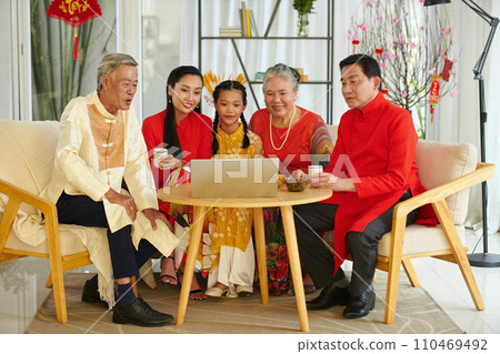 Big family gathered in front of laptop to watch movie and have some tea with treats after celebrating Spring festival 110469492