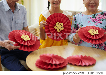 Joyful teenage girl and her grandparents making traditional paper decorations for Tet holiday Joyful teenage girl and her grandparents making traditional paper decorations for Tet holiday 110469591