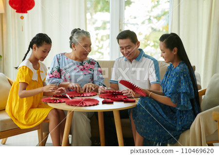 Three generation family making red paper fans to decorate house for Tet Three generation family making red paper fans to decorate house for Tet 110469620
