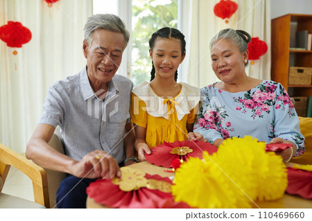 Grandparents teaching girl how to make red and yellow paper decorations for Tet 110469660