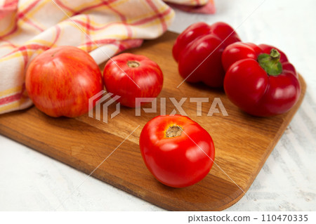 Cutting board with several red tomatoes and bell pepper on white wooden background with red kitchen towel.. Cutting board with several red tomatoes and bell pepper on white wooden background with red kitchen towel.. 110470335
