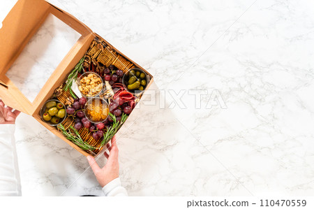Flat lay. Charcuterie box featuring sliced meat, cheese, crackers, and grapes, all neatly packaged in a brown gifting box. Flat lay. Charcuterie box featuring sliced meat, cheese, crackers, and grapes, all neatly packaged in a brown gifting box. 110470559