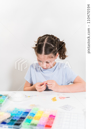 Little girl enjoys crafting colorful bracelets with vibrant clay beads set. Little girl enjoys crafting colorful bracelets with vibrant clay beads set. 110470594
