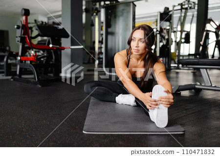 Woman is stretching body in gym. portrait and sport preparation. Young woman is stretching her leg in gym Woman is stretching body in gym. portrait and sport preparation. Young woman is stretching her leg in gym 110471832