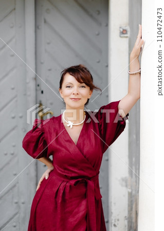 Attractive girl with hairstyle, in red dress is walking on street on old building background 110472473