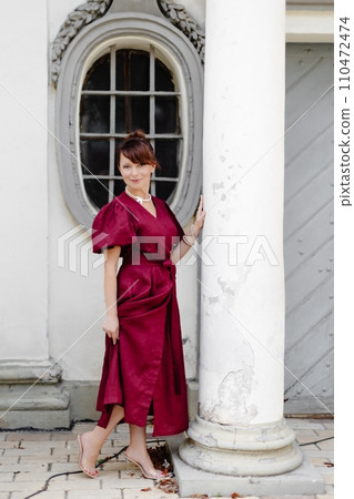 Attractive girl with hairstyle, in red dress is walking on street on old building background Attractive girl with hairstyle, in red dress is walking on street on old building background 110472474