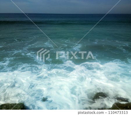 surf on shores of Indian ocean and overgrown with algae stones 110473313
