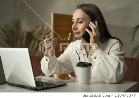 Woman is eating a cake sitting on the couch, drinking coffee. Beautiful woman in eating cake after a long day at work Woman is eating a cake sitting on the couch, drinking coffee. Beautiful woman in eating cake after a long day at work 110473377