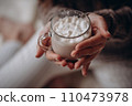 Transparent glass mug of cocoa with marshmallows in female hands. Close-up. New Year's portrait. 110473978