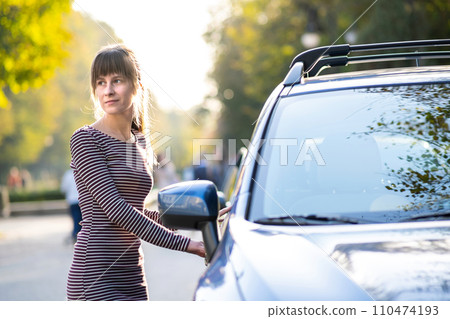 Young female driver resting near her car enjoying warm summer day. Travel and getaway concept. Young female driver resting near her car enjoying warm summer day. Travel and getaway concept. 110474193