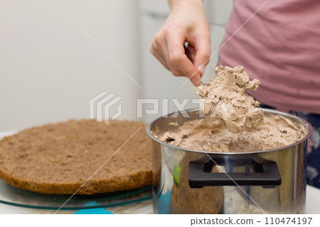 Working process of baking cake at home. Close up of female hand topping cream on chocolate biscuit. Culinary and delicious dessert concept. 110474197