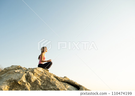 Woman hiker sitting on a steep big rock enjoying warm summer day. Young female climber resting during sports activity in nature. Active recreation in nature concept. 110474199