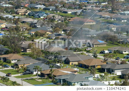 View from above of burning private house on fire and firefighters extinguishing flames after short circuit caused to ignite roof damaged by hurricane Ian wind. Home disaster in Florida suburban area 110474241
