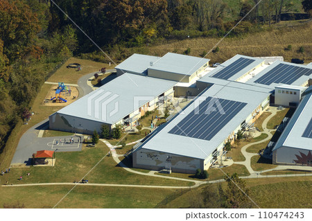 View from above of american school campus with roof covered with photovoltaic solar panels for producing of electrical clean energy View from above of american school campus with roof covered with photovoltaic solar panels for producing of electrical clean energy 110474243