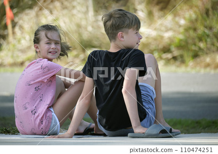 Two happy smiling teenage children, boy and girl sitting outdoors resting, having fun on summer sunny day 110474251