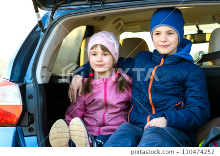 Two happy children boy and girl sitting together in a car trunk. Cheerful brother and sister hugging each other in family vehicle luggage compartment. Weekend travel and holidays concept. 110474252