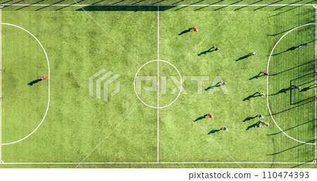 Top down aerial view of green football sports field and players playing football. Drone taken image of small unrecognizable sportsmen on grass covered stadium during sport activities. 110474393
