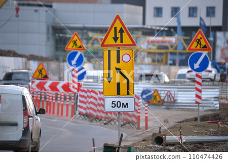 Roadworks warning traffic signs of construction work on city street and slowly moving cars Roadworks warning traffic signs of construction work on city street and slowly moving cars 110474426