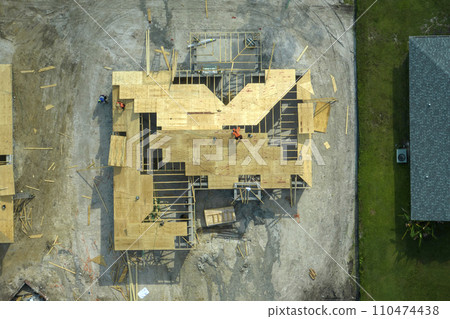 Professional builders working on roof construction of unfinished suburban home with wooden frame structure in Florida rural area. Concept of housing development in America Professional builders working on roof construction of unfinished suburban home with wooden frame structure in Florida rural area. Concept of housing development in America 110474438