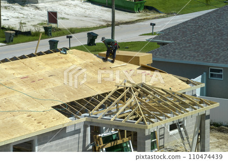 Professional builders working on roof construction of unfinished suburban home with wooden frame structure in Florida rural area. Concept of housing development in America Professional builders working on roof construction of unfinished suburban home with wooden frame structure in Florida rural area. Concept of housing development in America 110474439