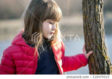 Portrait of a pretty child girl standing near a tree trunk in autumn outdoors. Portrait of a pretty child girl standing near a tree trunk in autumn outdoors. 110474525