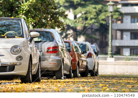 Modern cars parked on city street side in residential discrict. Shiny vehicles parked by the curb. Urban transportation infrastructure concept. Modern cars parked on city street side in residential discrict. Shiny vehicles parked by the curb. Urban transportation infrastructure concept. 110474549