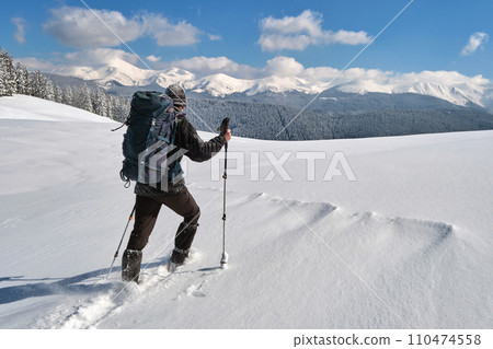 Man backpacker hiking snowy mountain hillside on cold winter day. 110474558