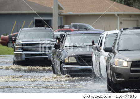 Hurricane flooded street with moving cars and surrounded with water houses in Florida residential area. Consequences of natural disaster 110474636