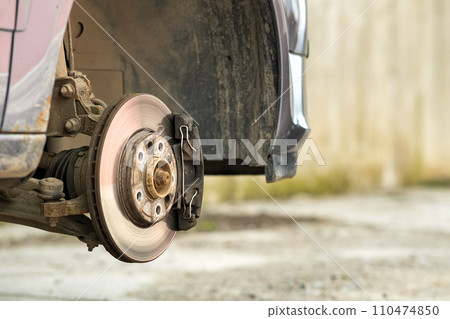 Closeup of braking disc of the vehicle with brake caliper for repair in process of new tire replacement. Car brake repairing in garage. Closeup of braking disc of the vehicle with brake caliper for repair in process of new tire replacement. Car brake repairing in garage. 110474850