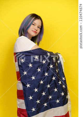 Proud Citizen With Multicolored Hair Poses For Camera In Studio, Wrapped In American Flag On Yellow Background. Patriotism, Pride, And Celebration Of Cultural Diversity. Proud American Teenager. High 110474874