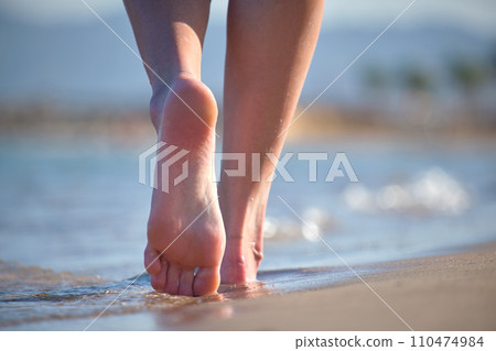 Close up of female feet walking barefoot on white grainy sand of golden beach on blue ocean water background Close up of female feet walking barefoot on white grainy sand of golden beach on blue ocean water background 110474984