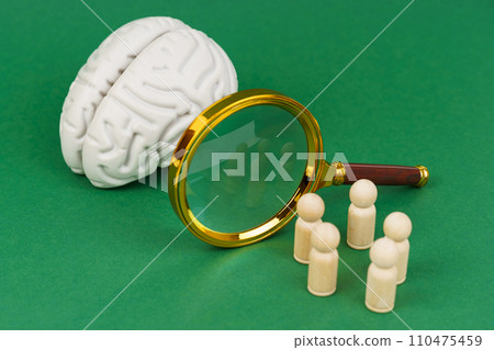 On a white background, a model of the brain, a magnifying glass and wooden human figures. 110475459