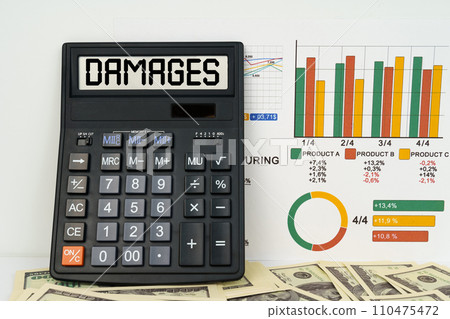 On the table are financial reports, dollars and a calculator with the inscription - damages On the table are financial reports, dollars and a calculator with the inscription - damages 110475472