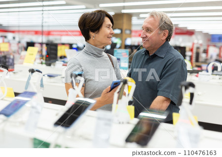 Mature couple diligently choosing smartphone in hypermarket Mature couple diligently choosing smartphone in hypermarket 110476163