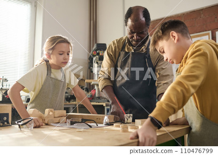 Waist up shot of male carpenter with two children building wooden toys together in crafting workshop 110476799