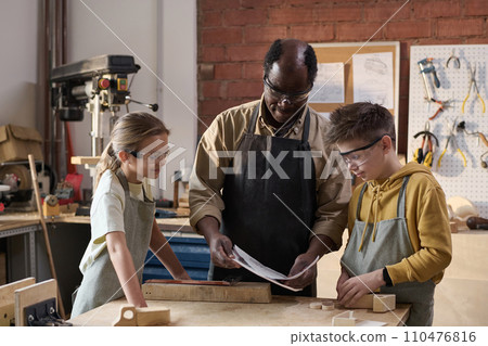 Waist up shot of African American man working on carpentry project with smiling children in workshop 110476816