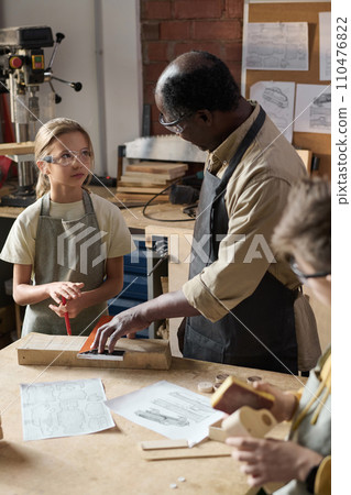Black senior man teaching carpentry class for children in workshop and looking at little girl 110476822