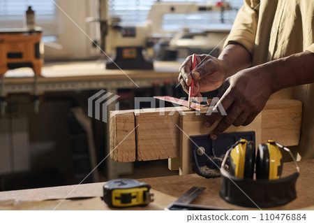 Side view closeup of senior carpenter measuring wood and building furniture in sunlit workshop 110476884