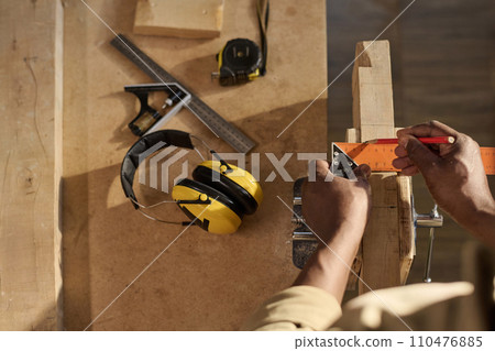 Closeup of unrecognizable carpenter measuring wood and building furniture at workstation in sunlight 110476885